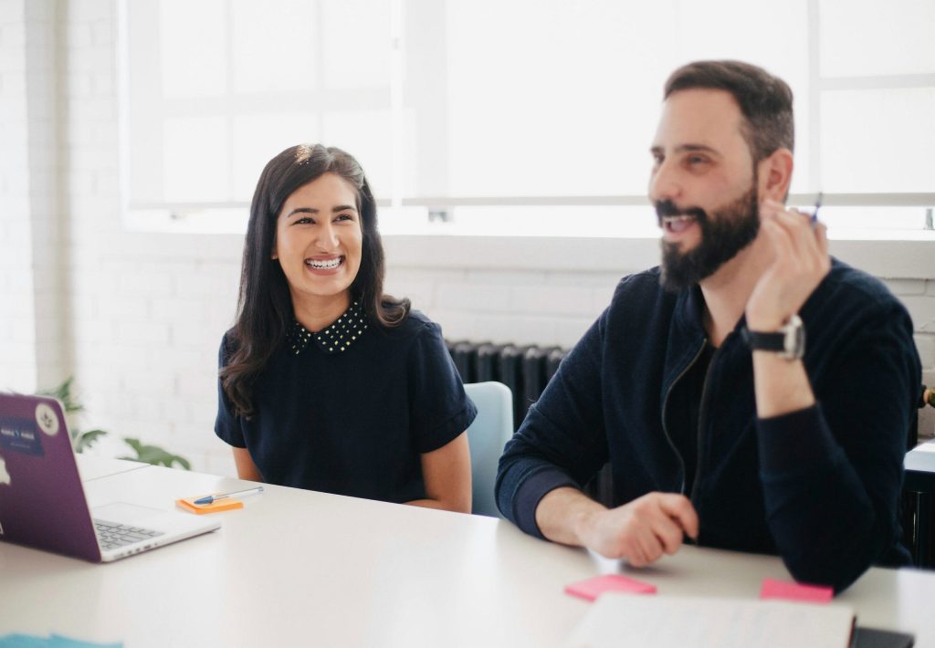 A man and woman smiling at the office together. They worked on improving office dynamics to create happy employees.